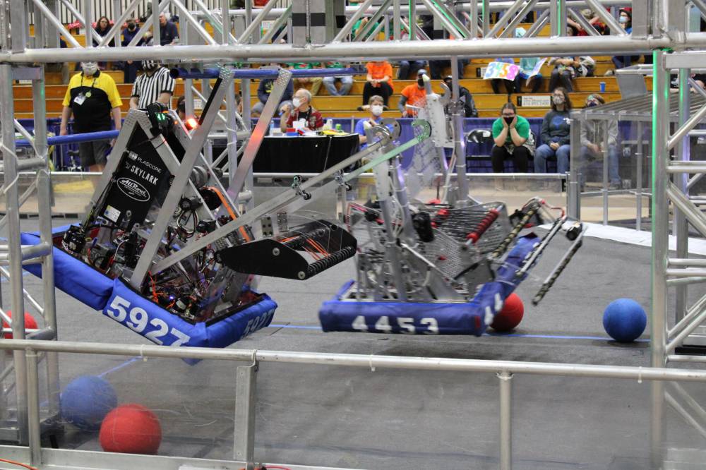 Two robots hang from a bar during a match
